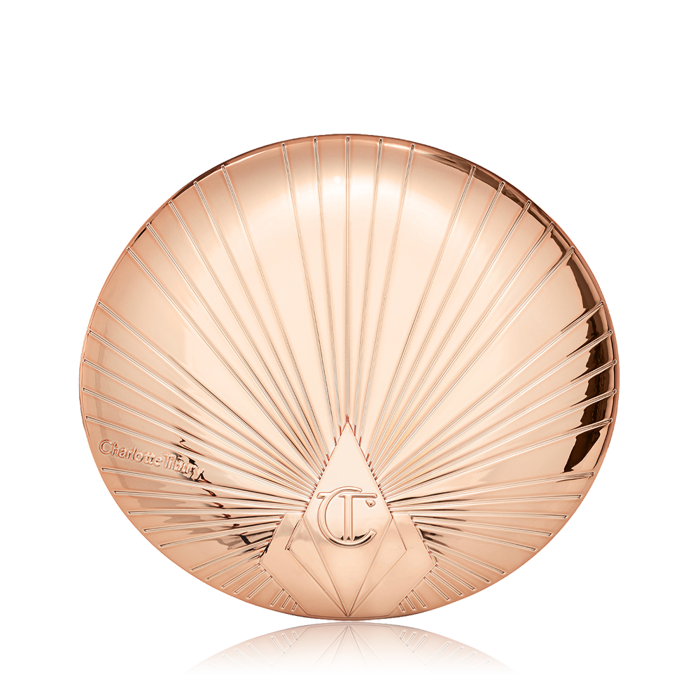 A closed, pressed powder compact in golden, metallic packaging with a starburst pattern on the lid. 